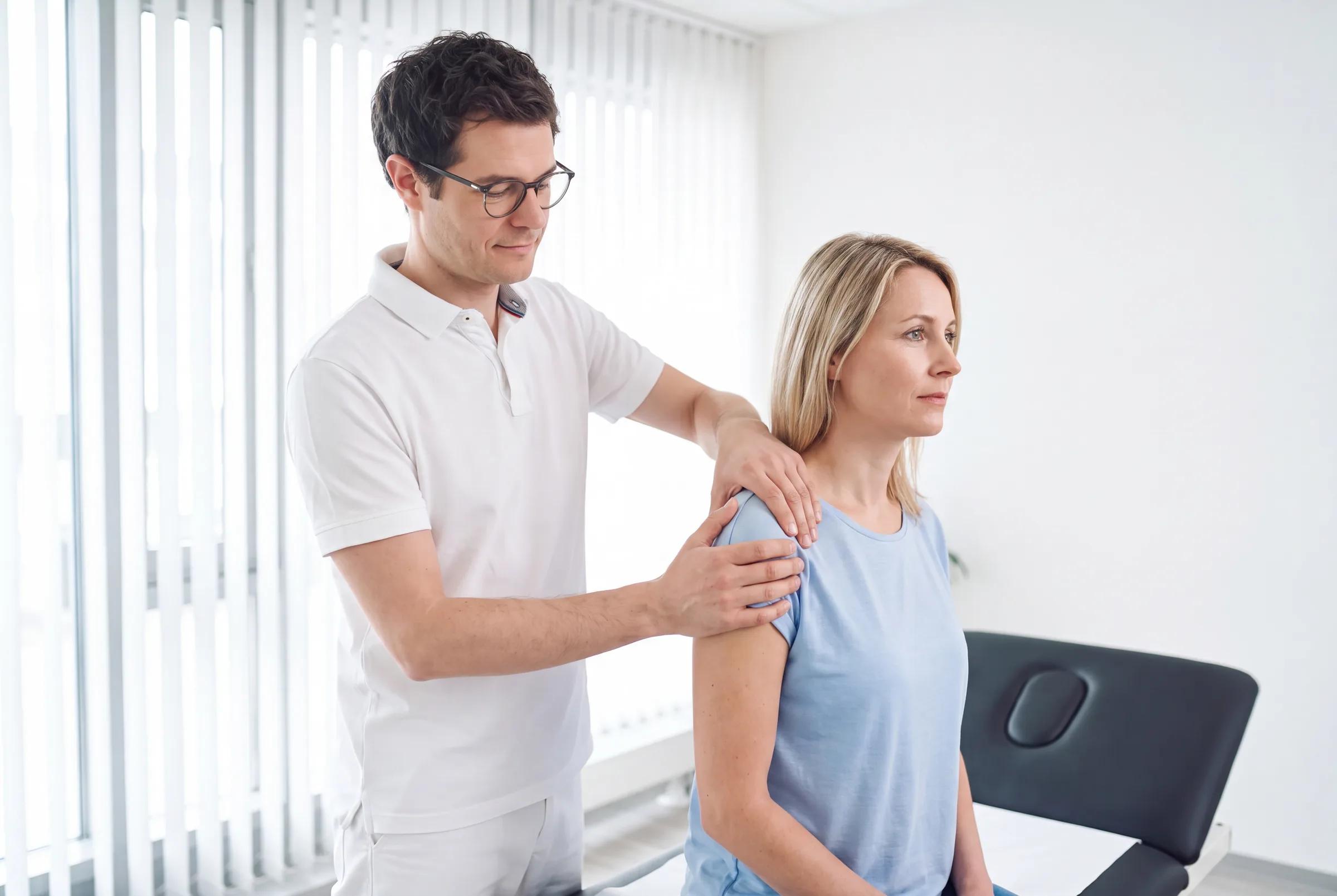 Orthopäde führt eine manuelle Behandlung der Schulter einer Patientin in der Praxis durch