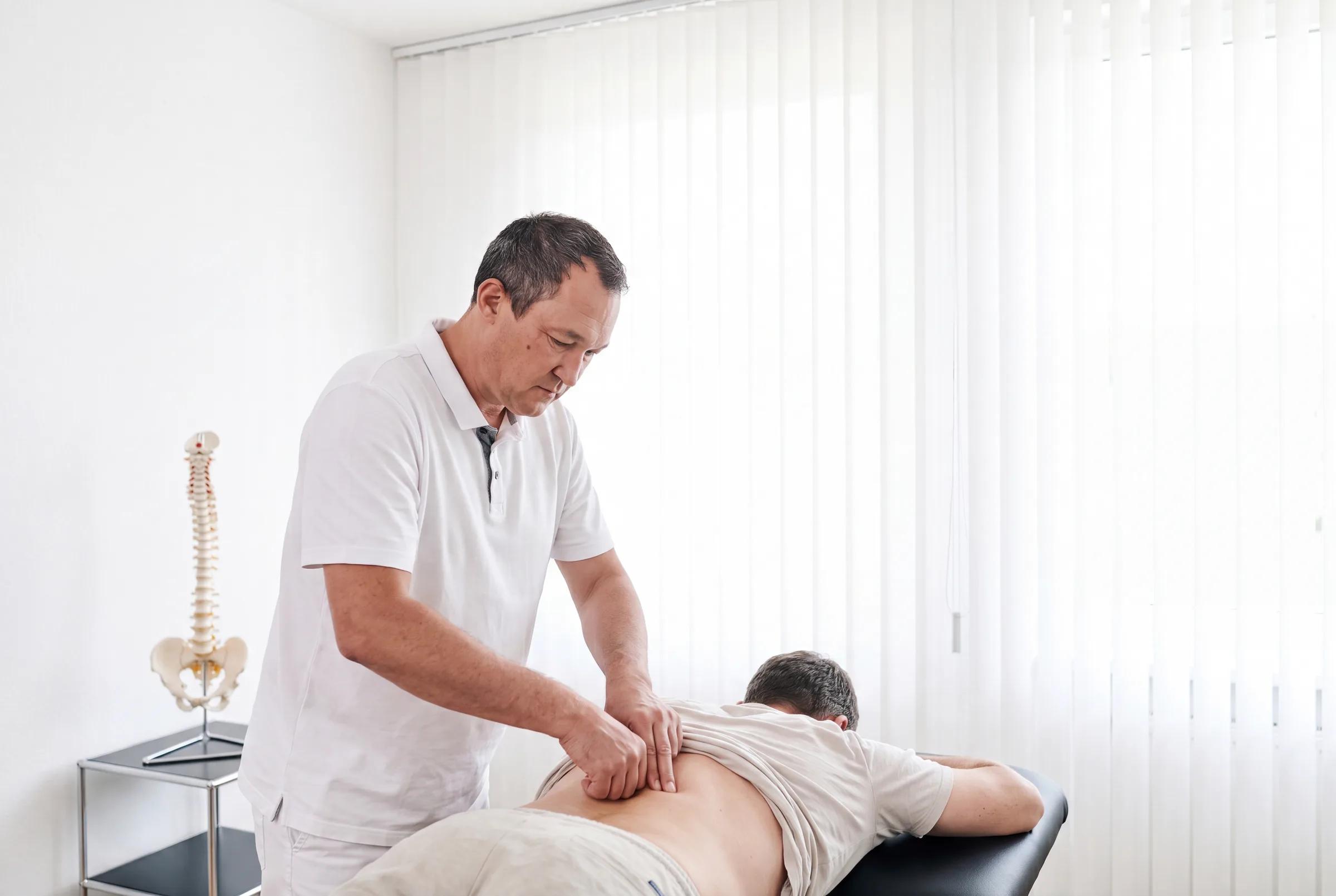 Orthopäde tastet die Wirbelsäule eines Patienten auf der Behandlungsliege ab