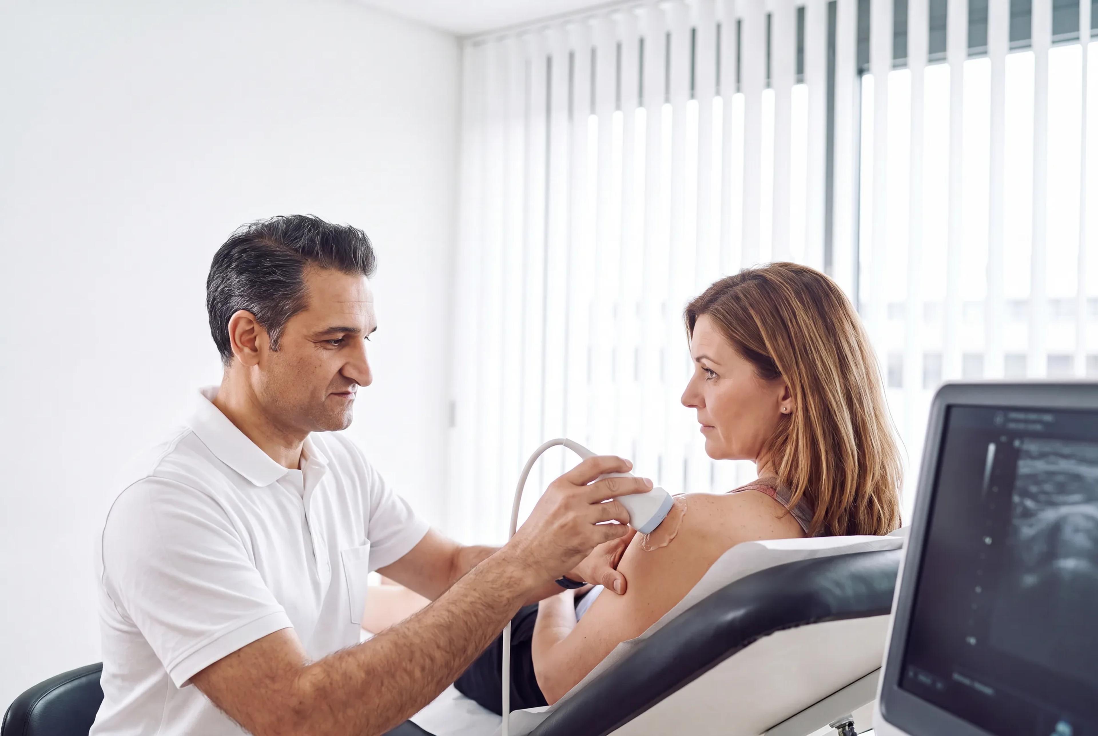 Orthopäde führt eine Ultraschalluntersuchung (Sonographie) der Schulter einer Patientin durch