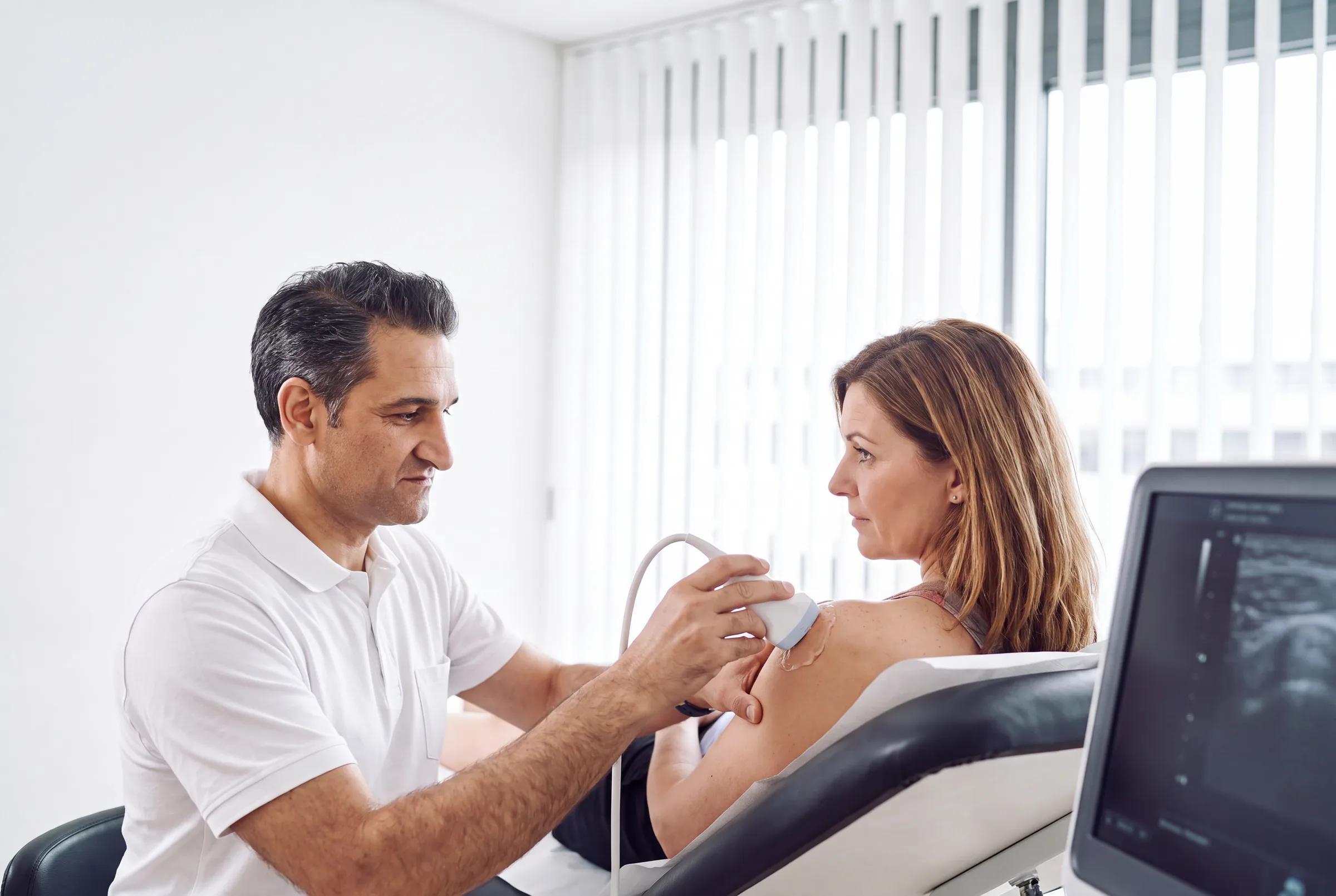 Orthopäde führt eine Ultraschalluntersuchung (Sonographie) der Schulter einer Patientin durch