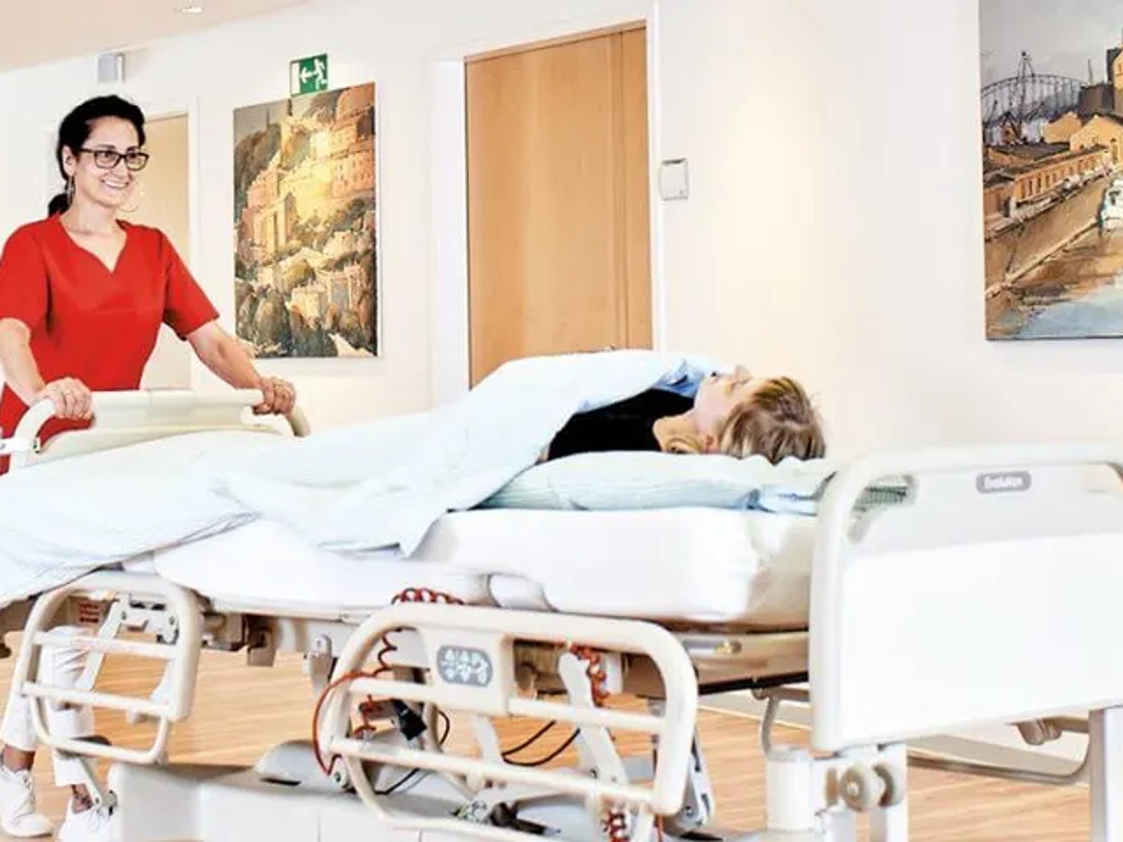 Eine medizinische Fachangestellte schiebt eine Patientin der Orthopädie Mediapark in ihrem Bett durch die Klinik.