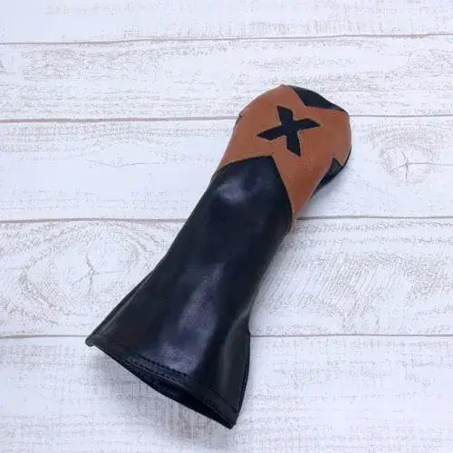 ブラックとブラウンのツートンカラーのゴルフクラブ用ヘッドカバー。上部のブラウン部分には黒い「X」マークがデザインされており、カバー全体がシンプルでエレガントなスタイル。背景は白木目のテクスチャが施された表面。