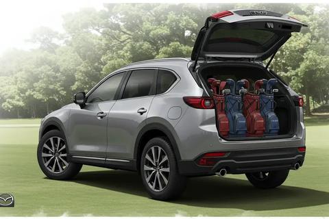 ゴルフ場の駐車エリアで停車するヴォクシー。開いたテールゲート付近に4つのゴルフバッグが見え、余裕ある積載感を示す。中〜遠景、自然光で落ち着いたクールトーン。ロゴは画像の端に小さく配置(車・バッグ上は不可)。