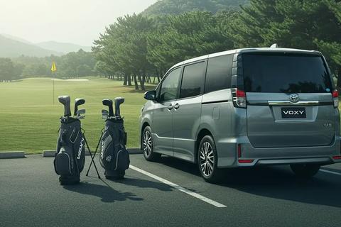 ゴルフ場の駐車エリアで停車するヴォクシー。開いたテールゲート付近に4つのゴルフバッグが見え、余裕ある積載感を示す。中〜遠景、自然光で落ち着いたクールトーン。ロゴは画像の端に小さく配置(車・バッグ上は不可)。