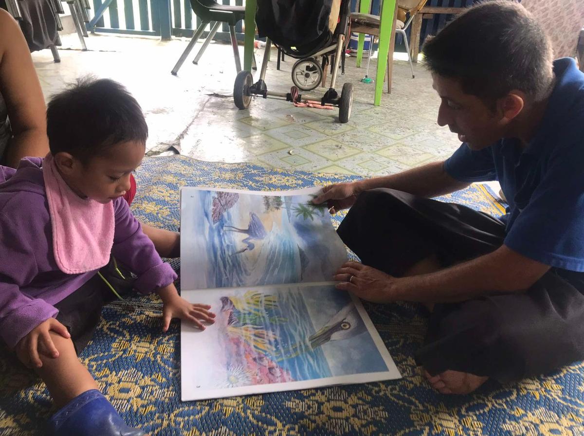 A man and child seated on the floor reading a picture book together A man and child seated on the floor reading a picture book together