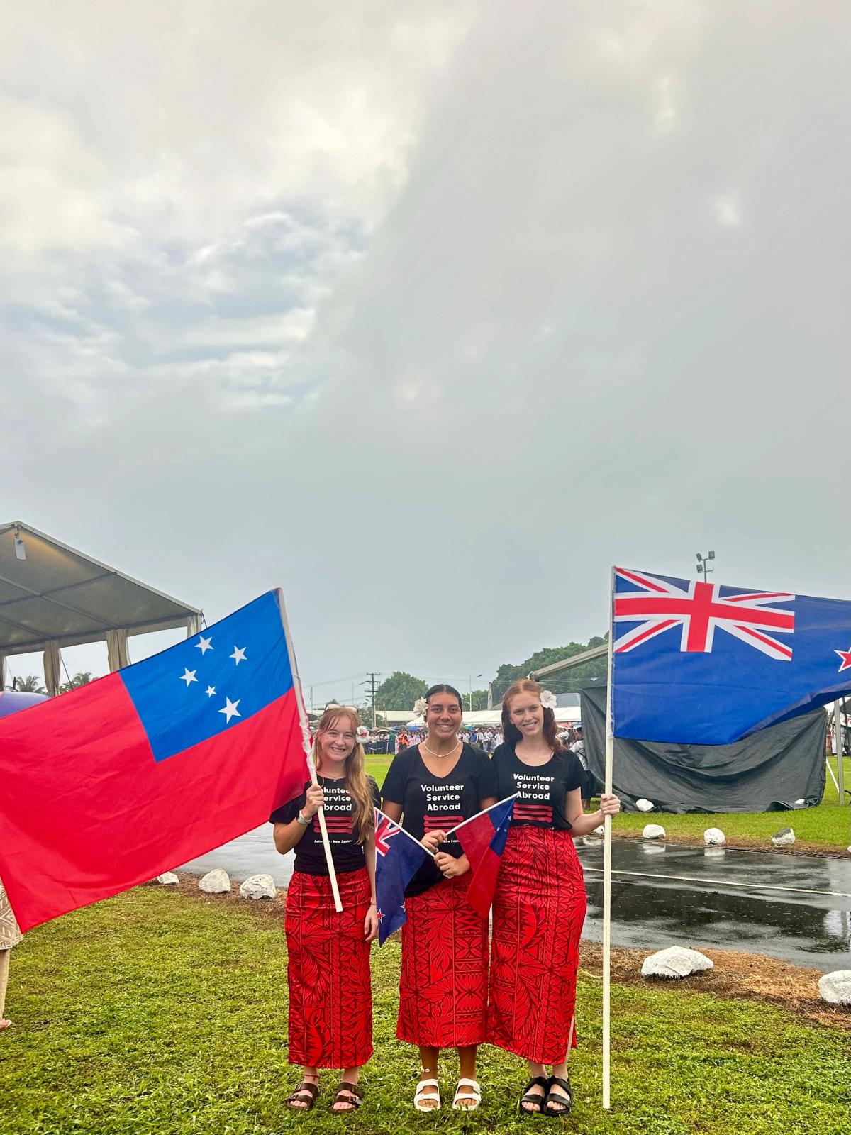 Three young women smile for the camera while holding the Samoan and New Zealand flags Three young women smile for the camera while holding the Samoan and New Zealand flags