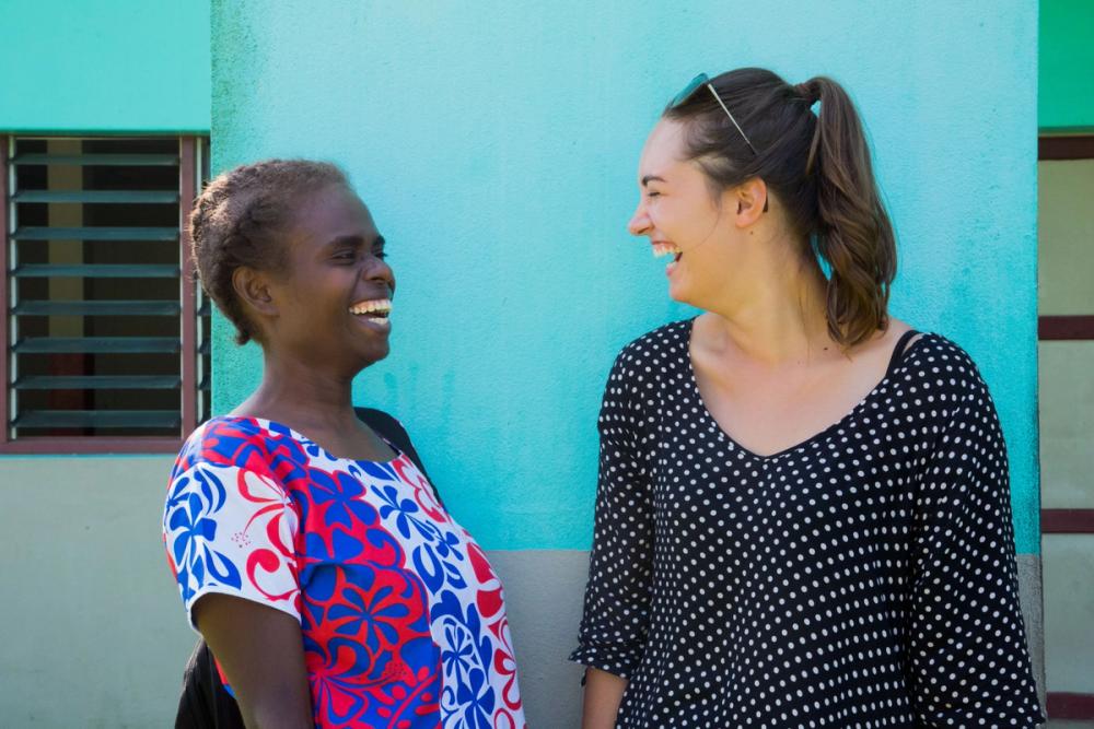two women are standing next to each other and laughing in front of a blue wall .
