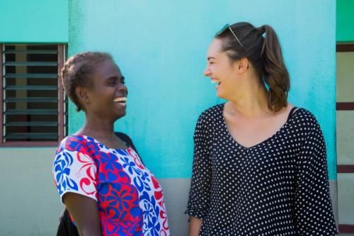 two women are standing next to each other and laughing in front of a blue wall .