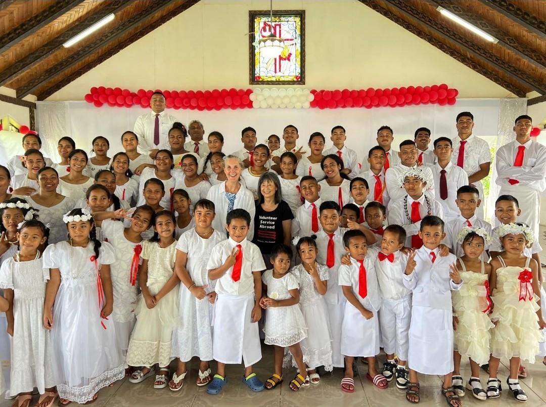 A large group of children dressed in white for White Sunday in Samoa, with two women in the middle of the group smiling for the camera. A large group of children dressed in white for White Sunday in Samoa, with two women in the middle of the group smiling for the camera.