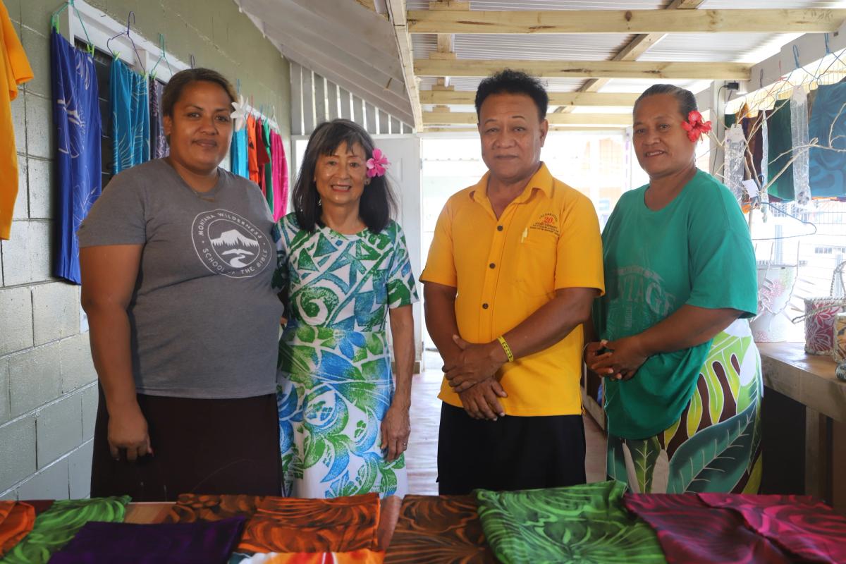 A group of people stand behind a clothing display at a market stall and smile for the camera A group of people stand behind a clothing display at a market stall and smile for the camera