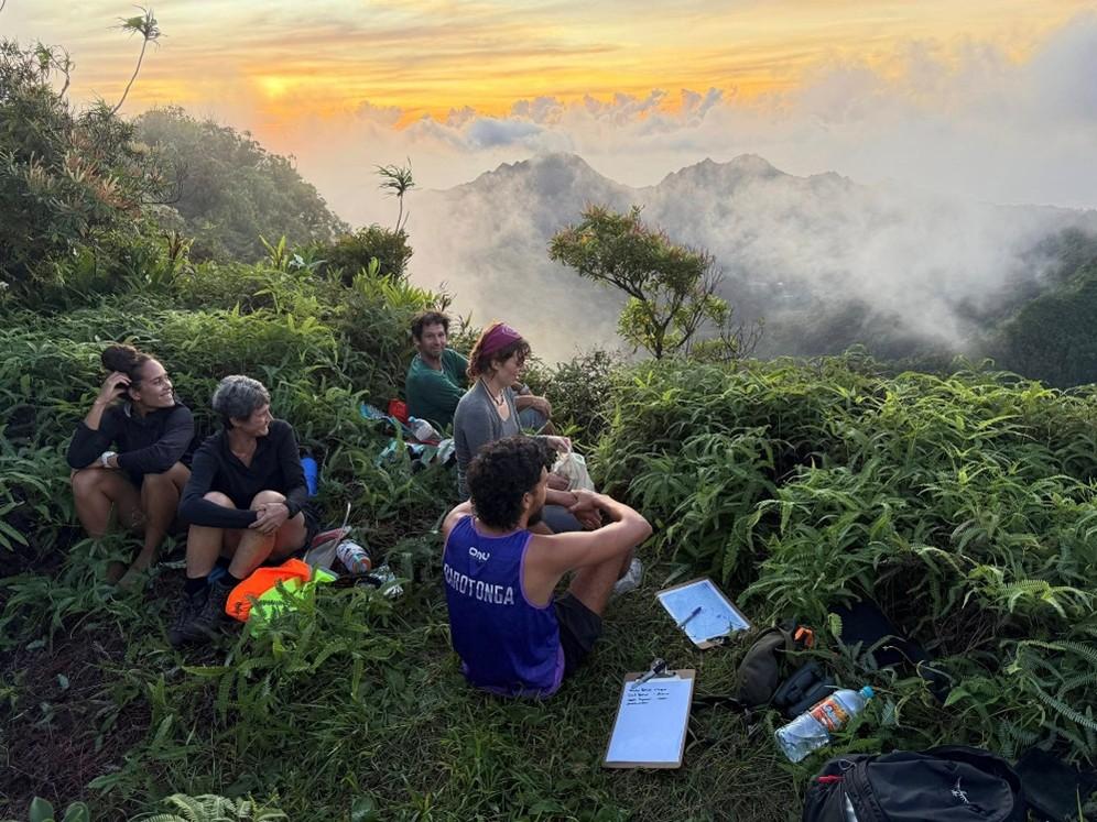 A group of people sit on top of a mountain looking at the view below A group of people sit on top of a mountain looking at the view below