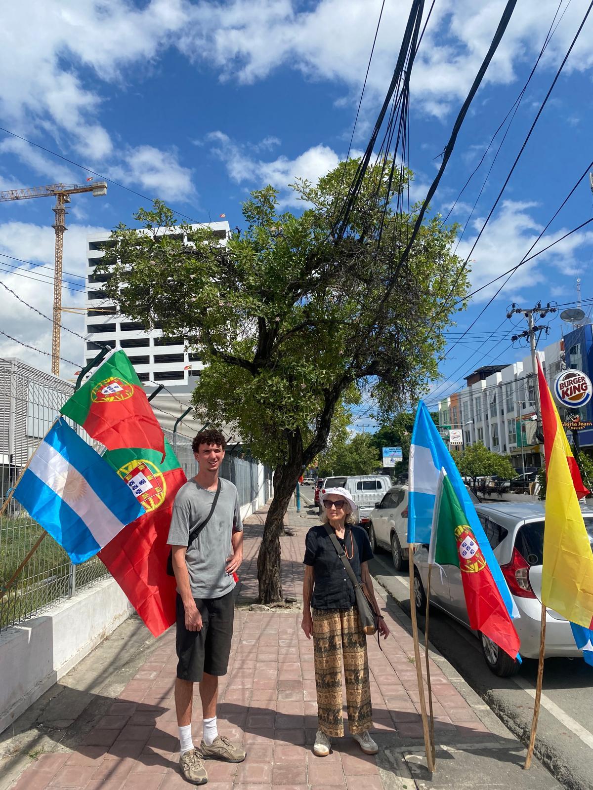 Two people walking on a street sidewalk between many flags.