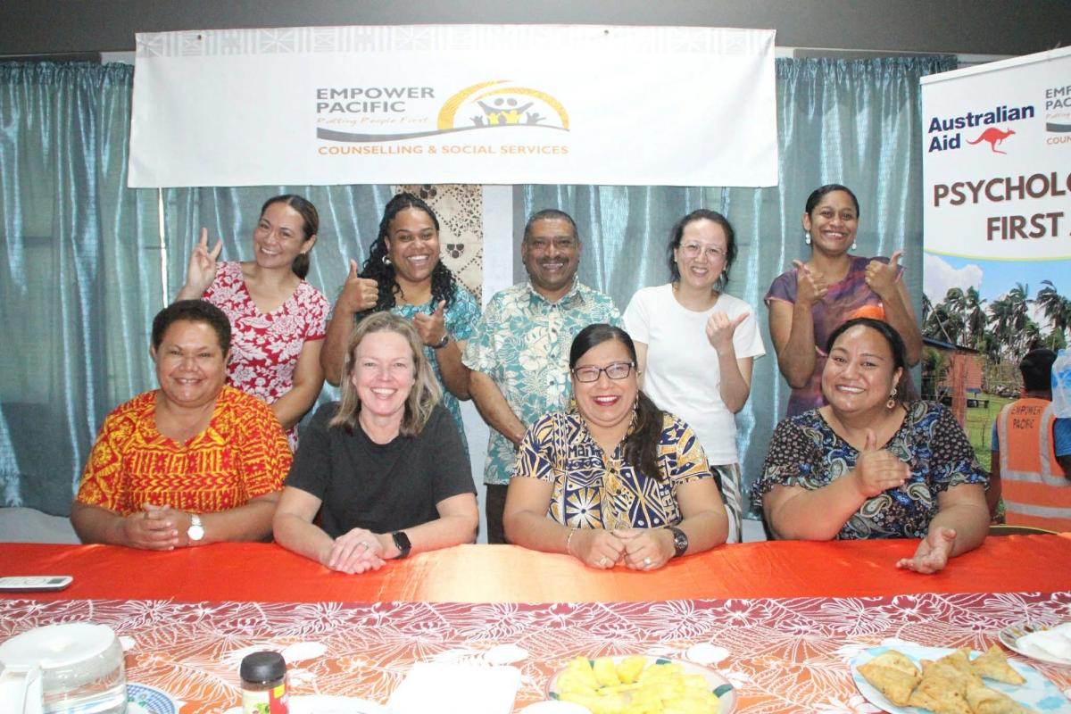 A group of people seated behind a table and smiling for the camera A group of people seated behind a table and smiling for the camera