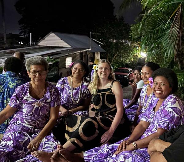 A group of women seated on the ground and smiling for the camera