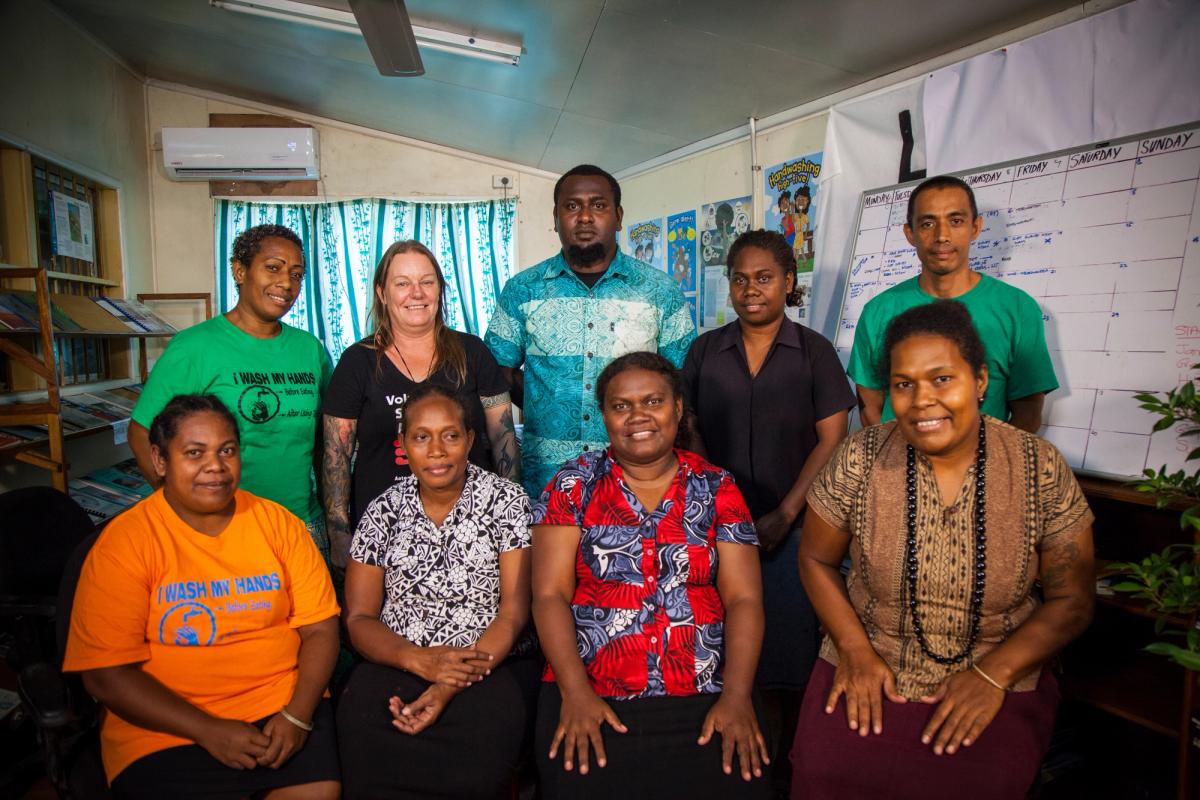 A group of people seated inside an office and smiling at the camera A group of people seated inside an office and smiling at the camera