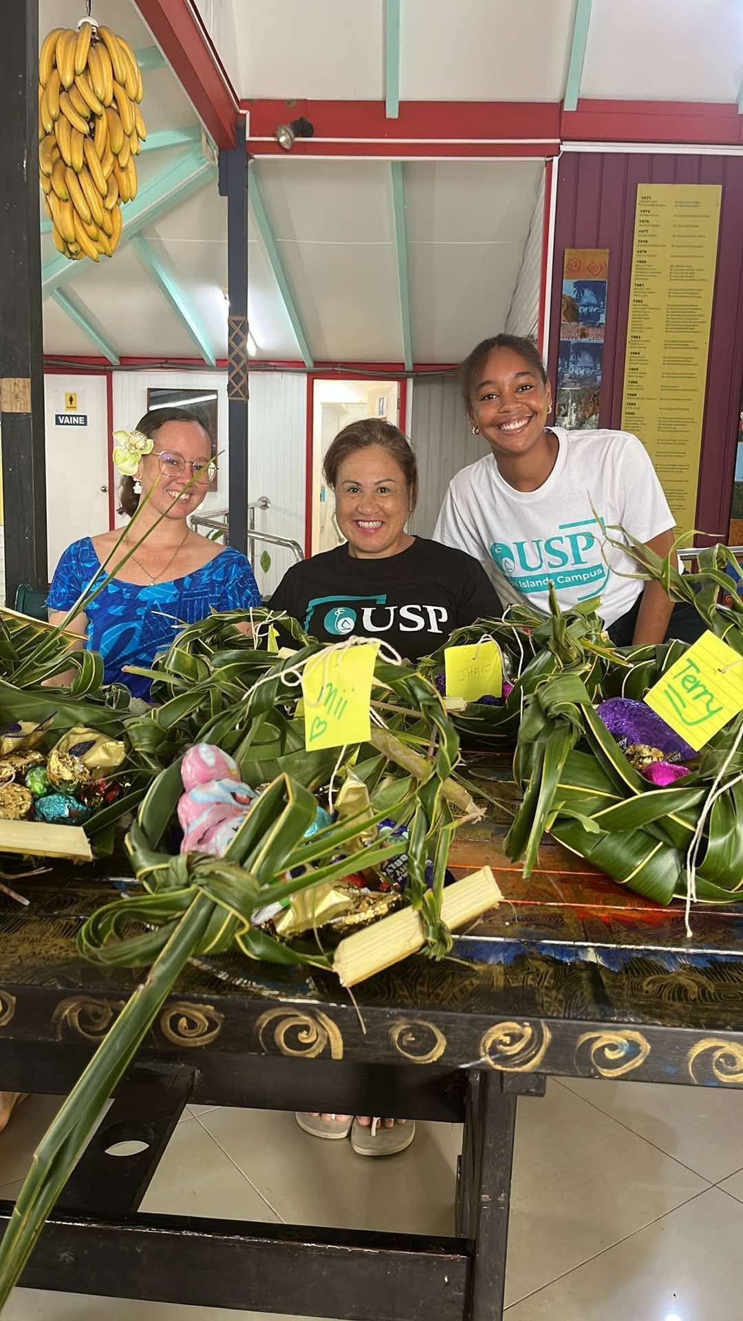 Three women smiling for the camera behind flax baskets.