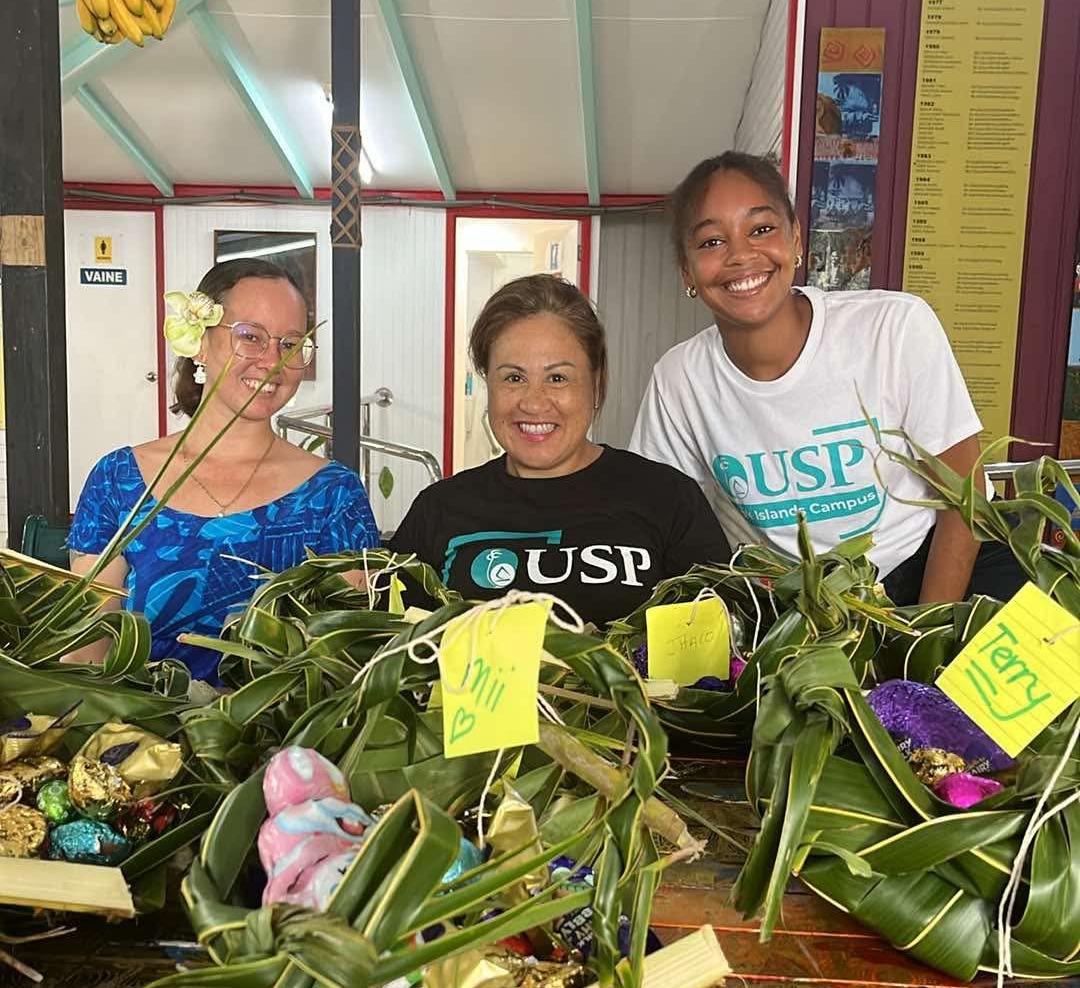 Three women smiling for the camera behind flax baskets. Three women smiling for the camera behind flax baskets.