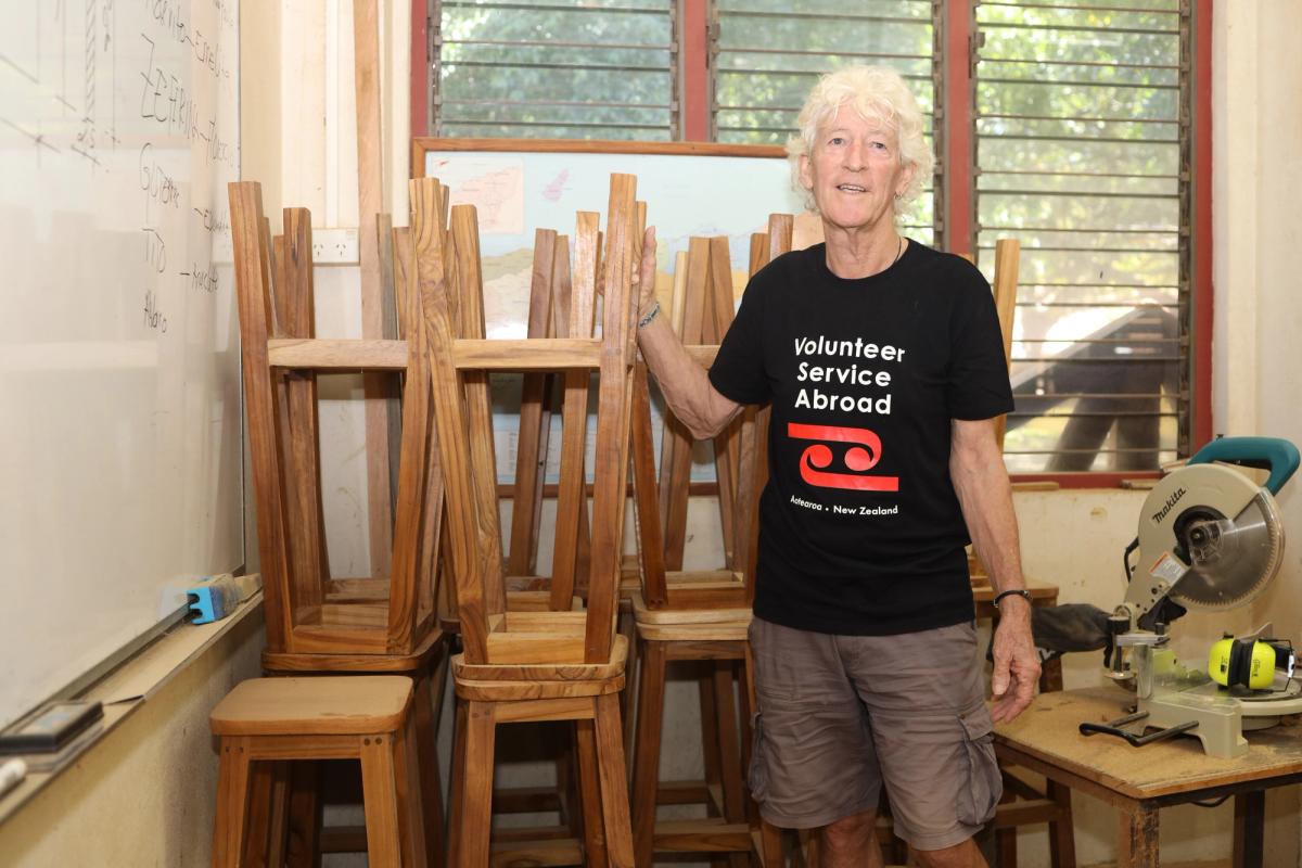A man stands in front of some stools made by some carpentry students.