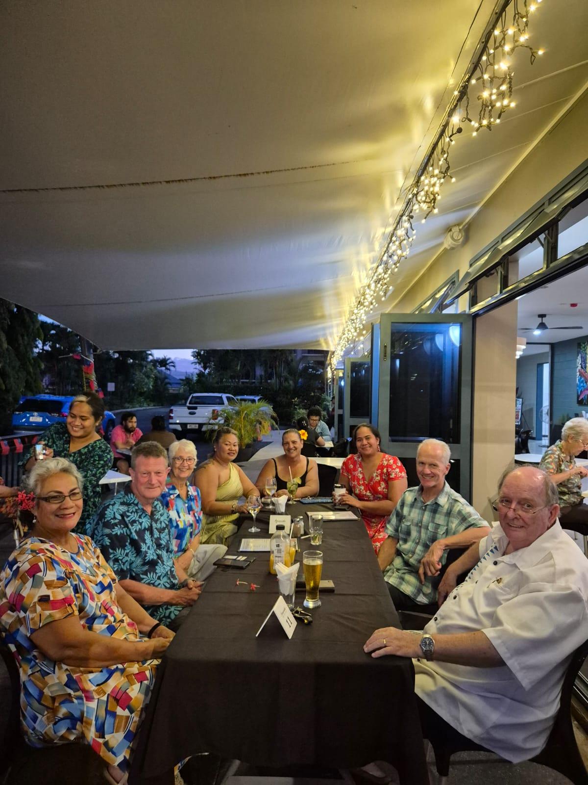 A group of people seated around a dinner table and smiling at the camera. A group of people seated around a dinner table and smiling at the camera.