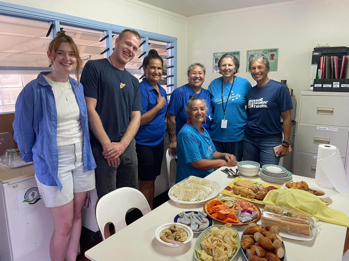 A group of people seated and standing by a table of food A group of people seated and standing by a table of food