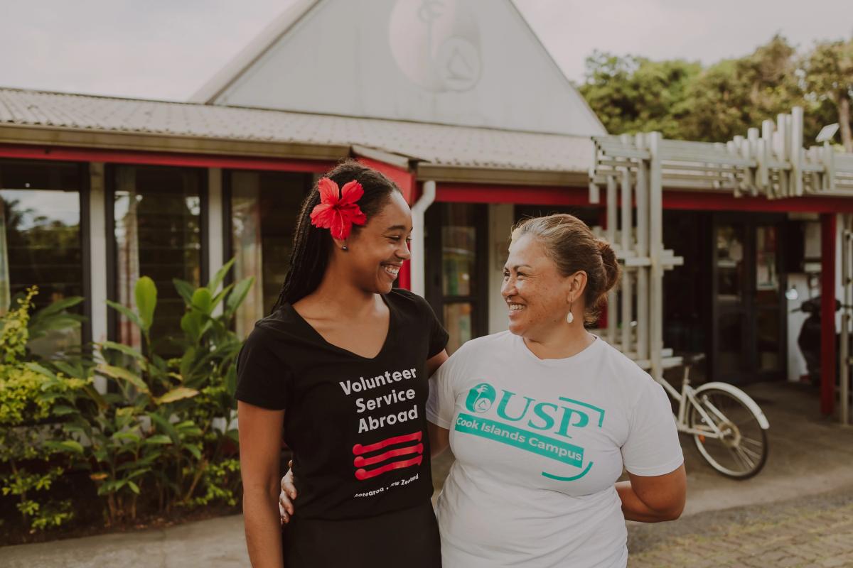 Two women stand side by side and smile at each other