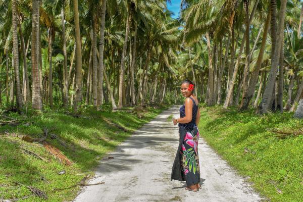 a woman is standing on a dirt road surrounded by palm trees . a woman is standing on a dirt road surrounded by palm trees .