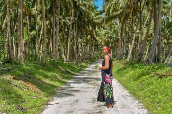 a woman is standing on a dirt road surrounded by palm trees .