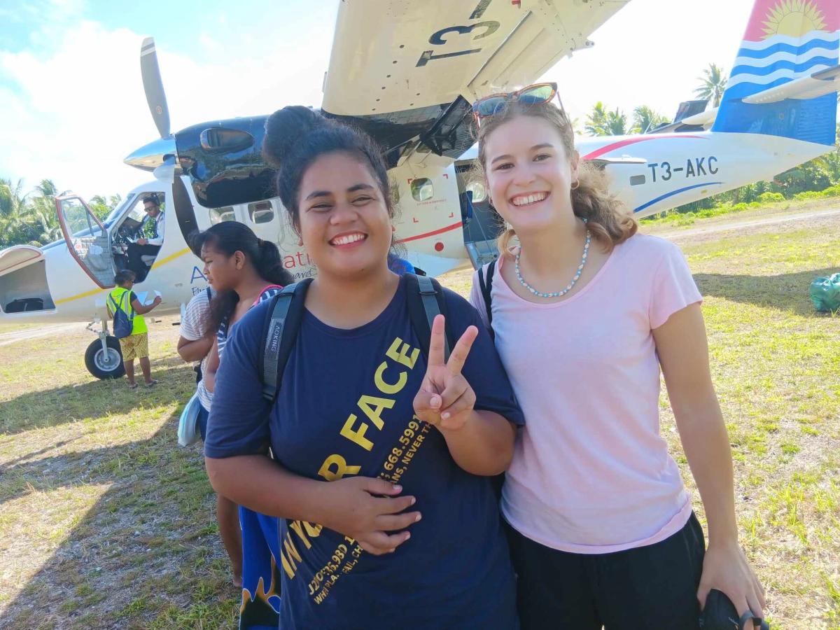 Two women standing in front of a plane and smiling for the camera