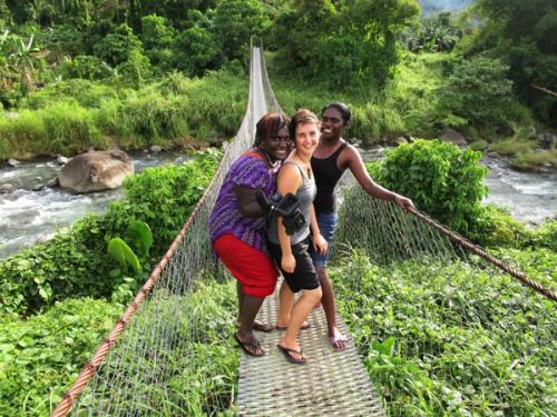 three people are standing on a rope bridge over a river .