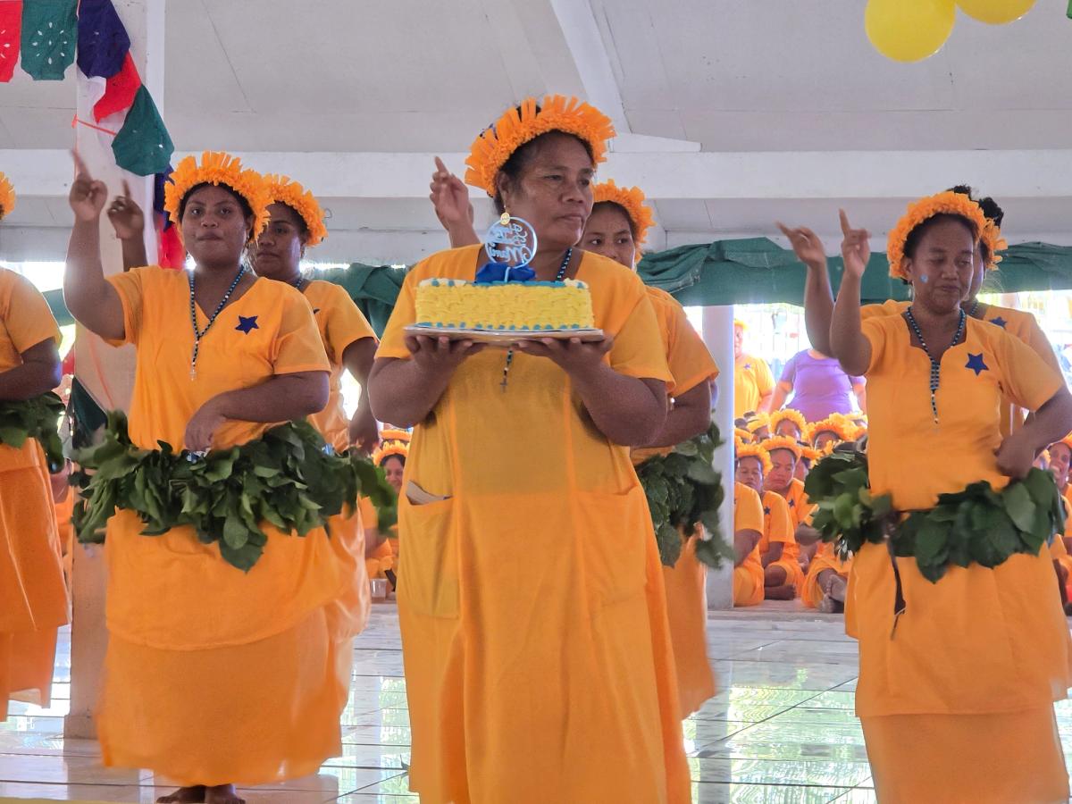 A women holds a birthday cake surrounded by other women dancing