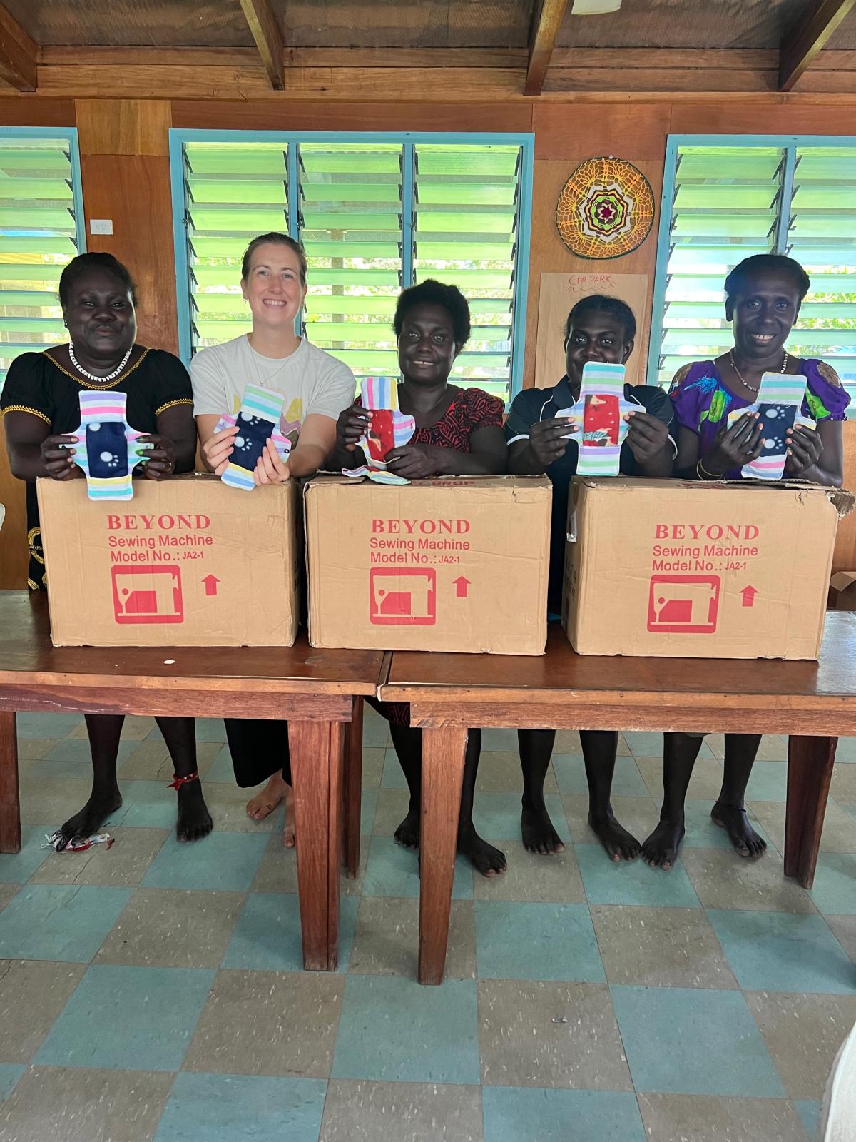 Women standing and smiling for the camera while holding the sanitary pads that they've just learnt to sew Women standing and smiling for the camera while holding the sanitary pads that they've just learnt to sew