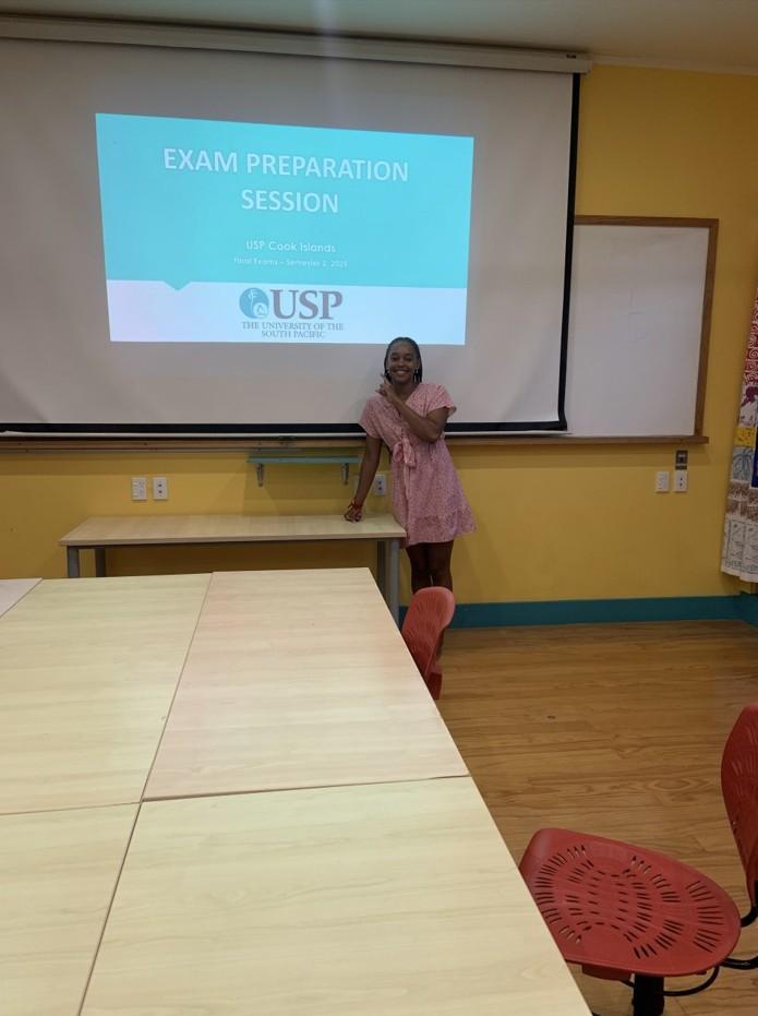 A young woman smiles and stands in front of a projector screen in a classroom. A young woman smiles and stands in front of a projector screen in a classroom.