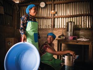 two women are standing next to each other in a kitchen holding bowls . two women are standing next to each other in a kitchen holding bowls .