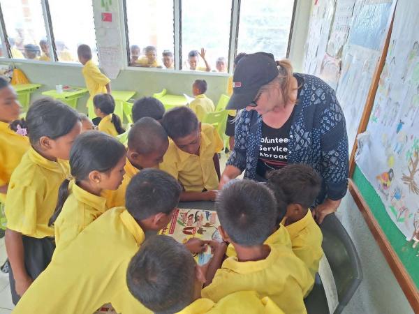 A woman and group of children huddled around a desk in a classroom. A woman and group of children huddled around a desk in a classroom.