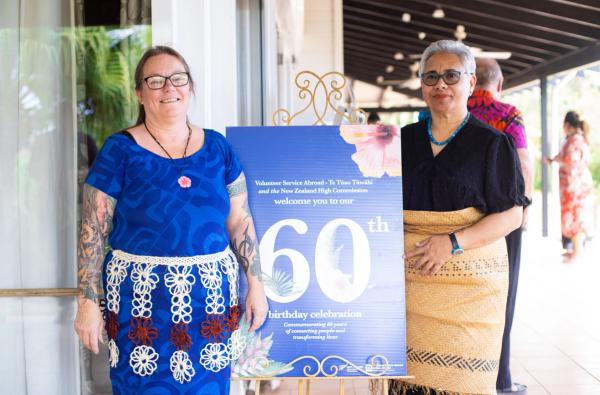 Two women stand next to a sign and smile for the camera.
