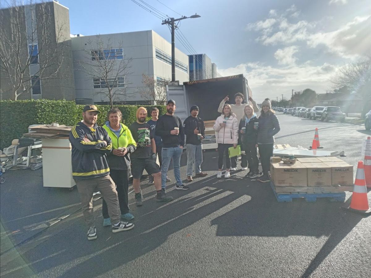 A group of people stand in front of a shipping container and smile for the camera A group of people stand in front of a shipping container and smile for the camera