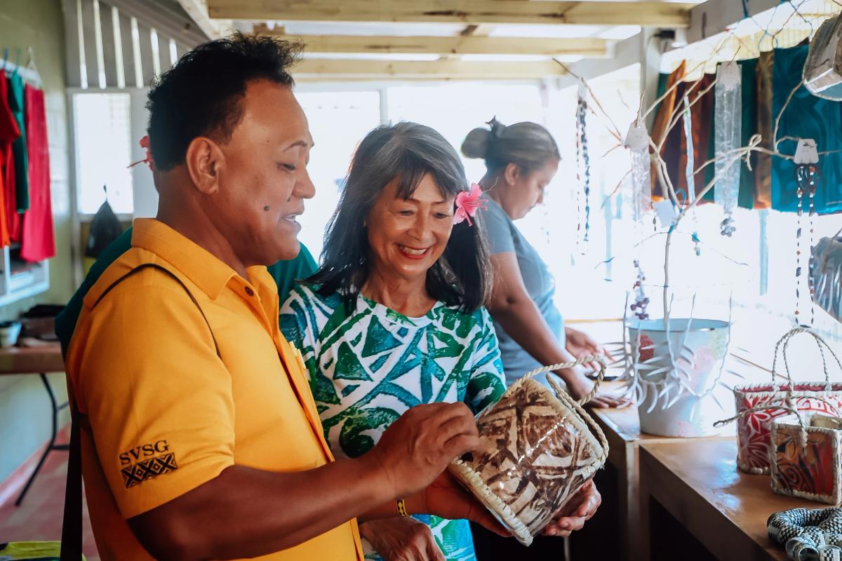 Two people stand and look at the details of a handbag in a market stall