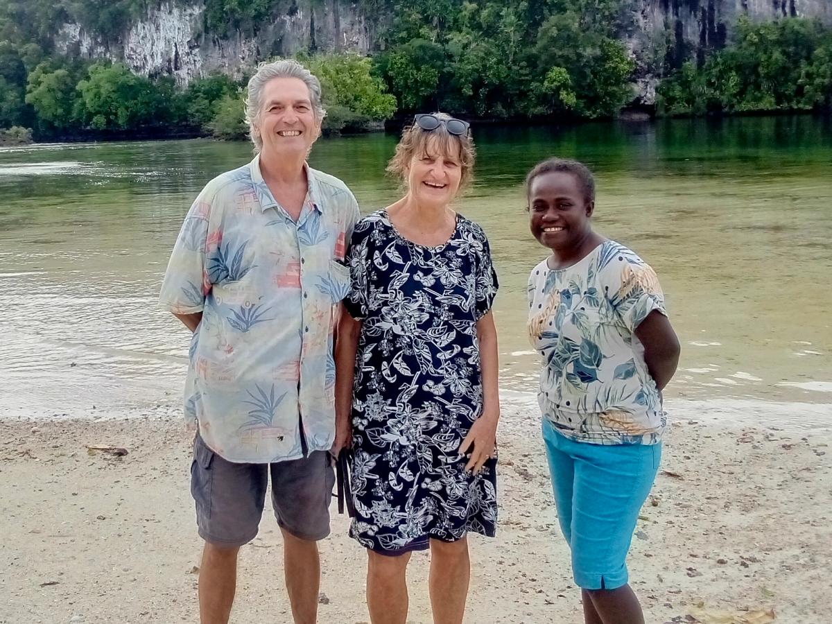 Three people stand in front of a body of water and smile for the camera