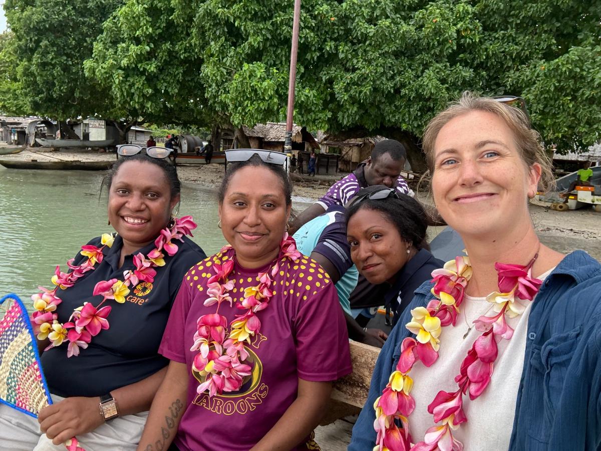 Four women smiling for the camera as they sit on a boat and have flower leis