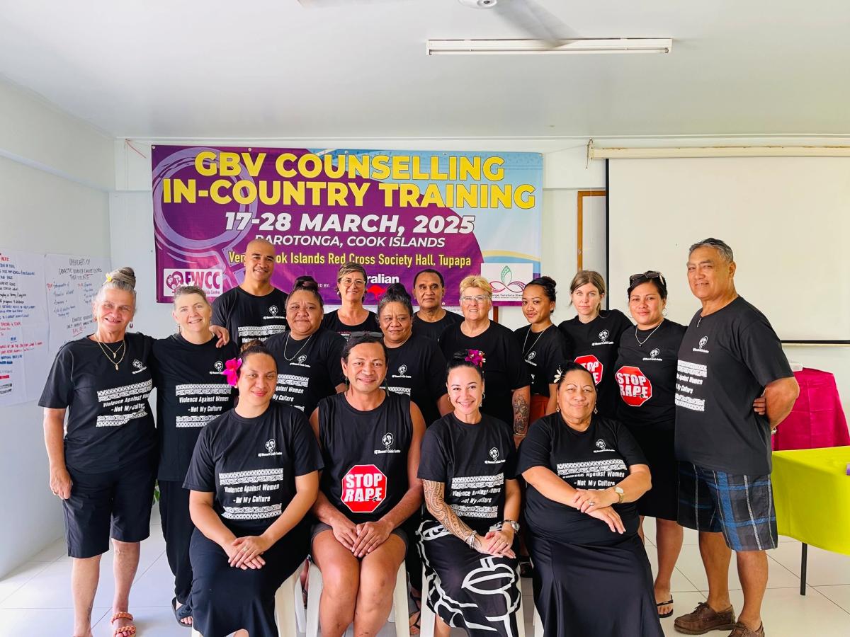 A group of people both seated and standing smile for the camera in front of a banner.