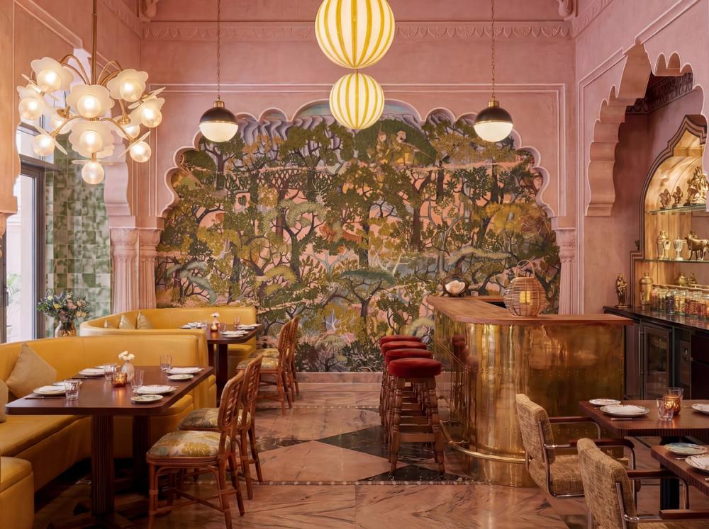 an interior photo of an Indian restaurant with a forest themed wallpaper mural and pink accents