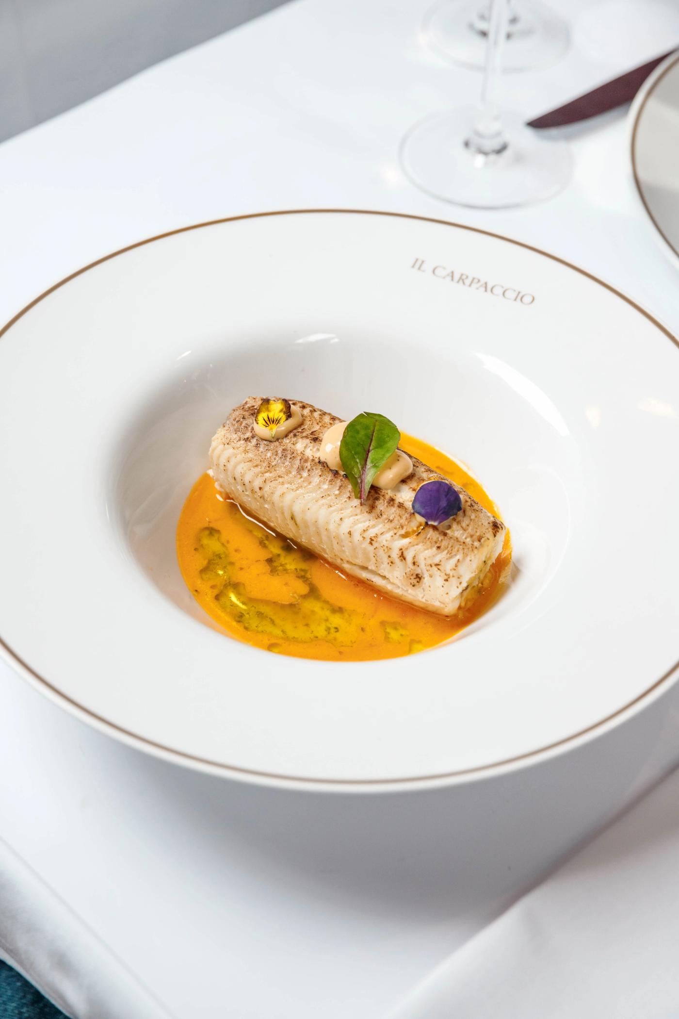 Elegant fish dish with edible flowers in a saffron sauce, served on Il Carpaccio's signature plate