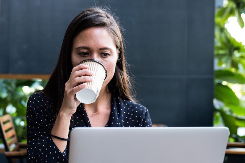 Woman working at computer on job CV with coffee - Image - She Mentors
