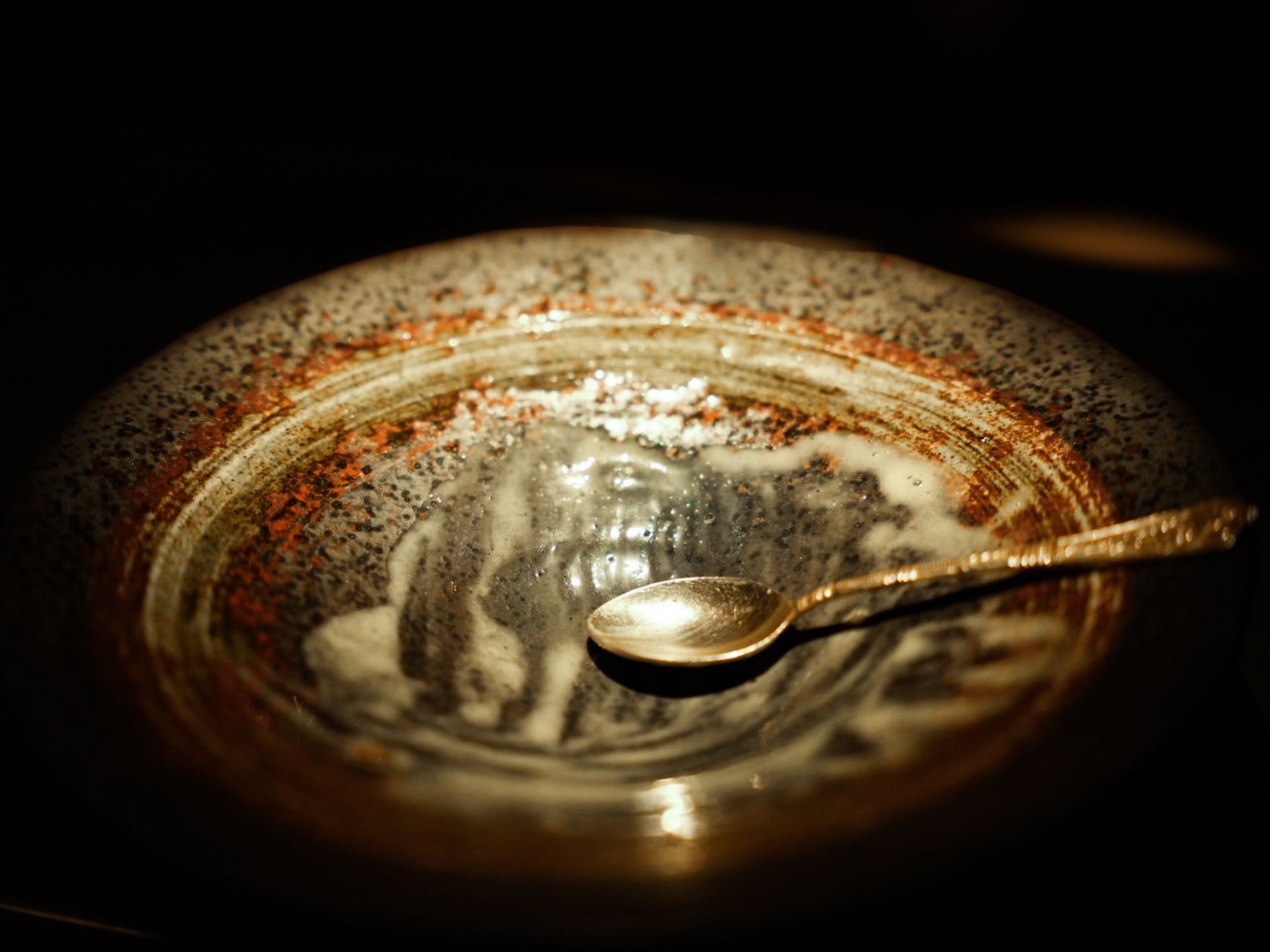 An antique spoon resting on a dark glazed ceramic bowl.