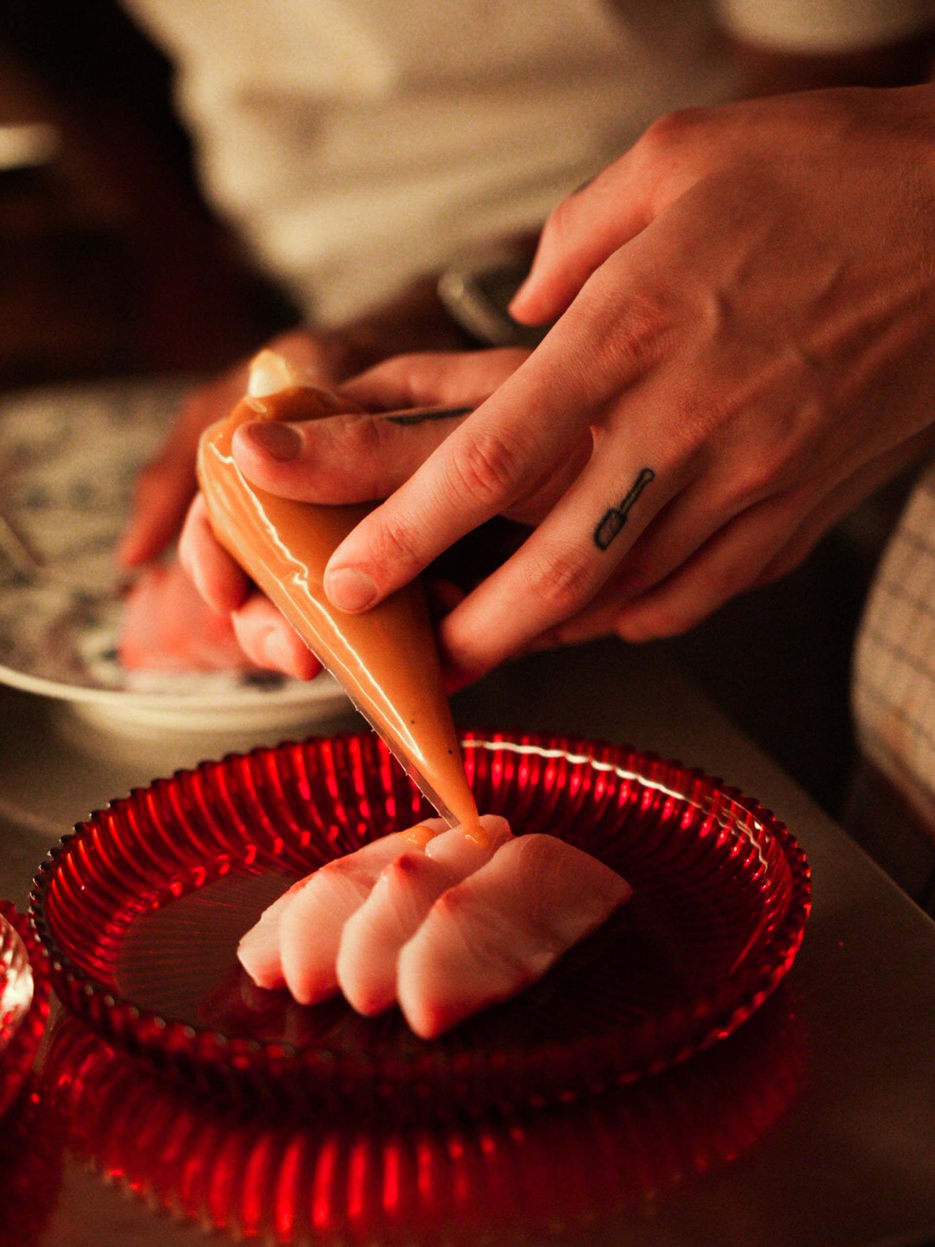 Hands piping caramel over a plated scallop.