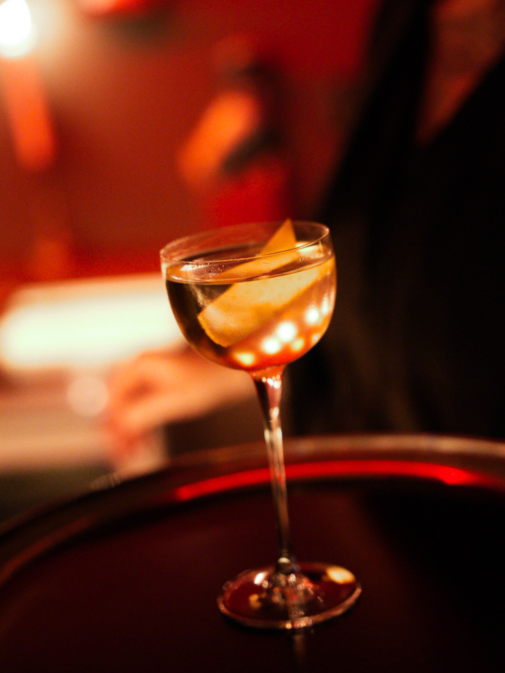 A coupe cocktail with a citrus twist, lit by candlelight.