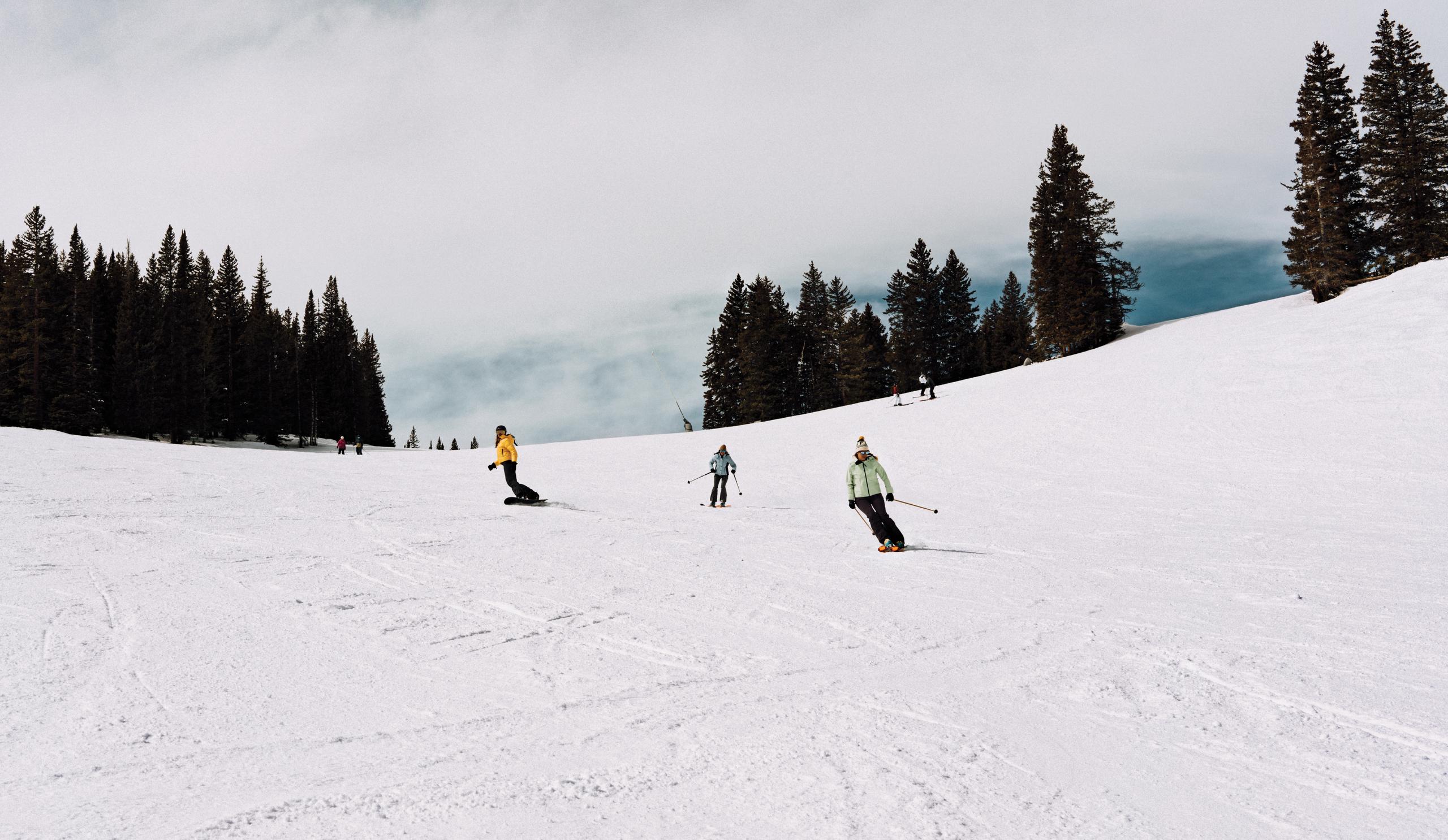Two women skiing and one woman snowboarding down mountain in Aspen, Colorado