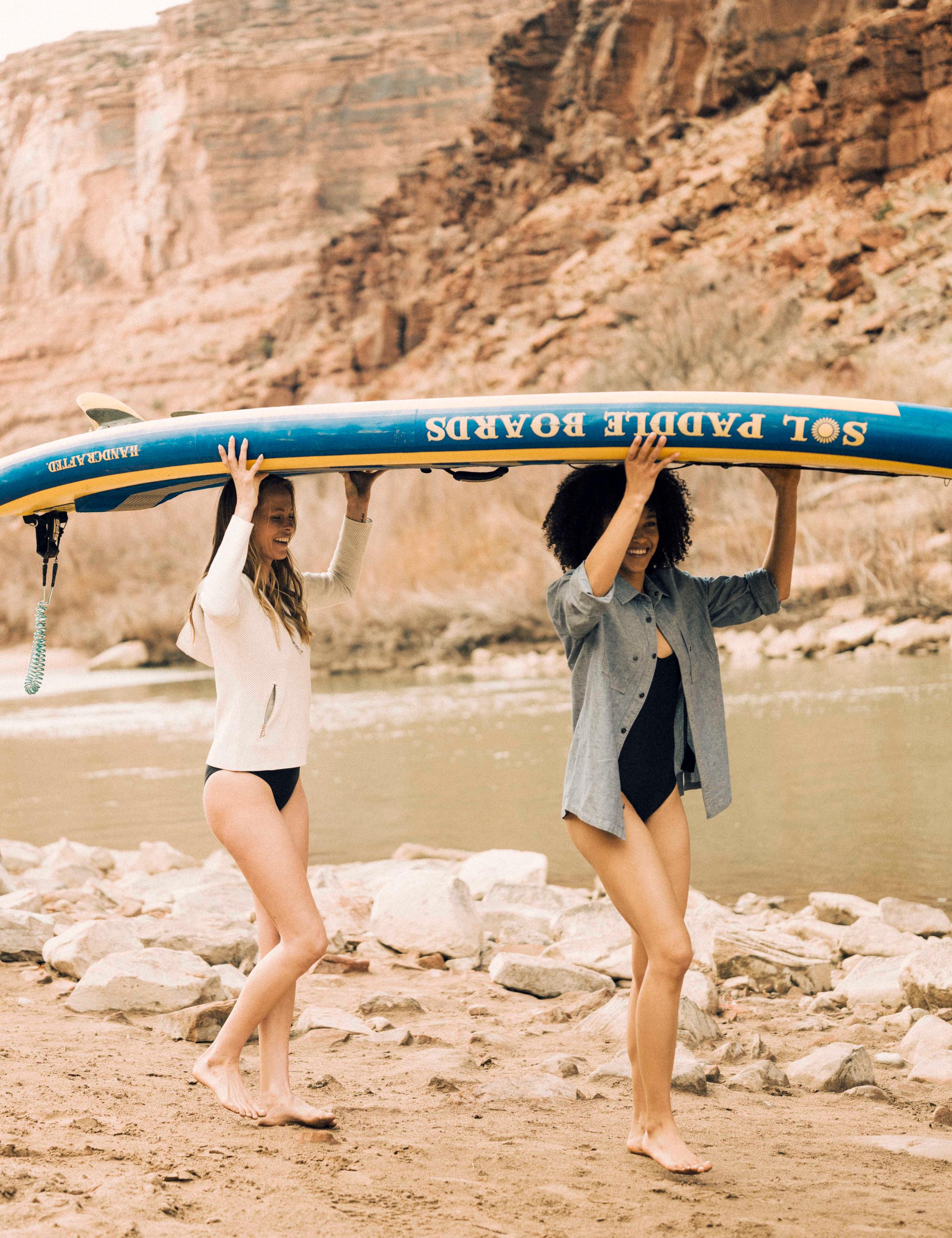 Two women carrying paddle board next to river in Utah