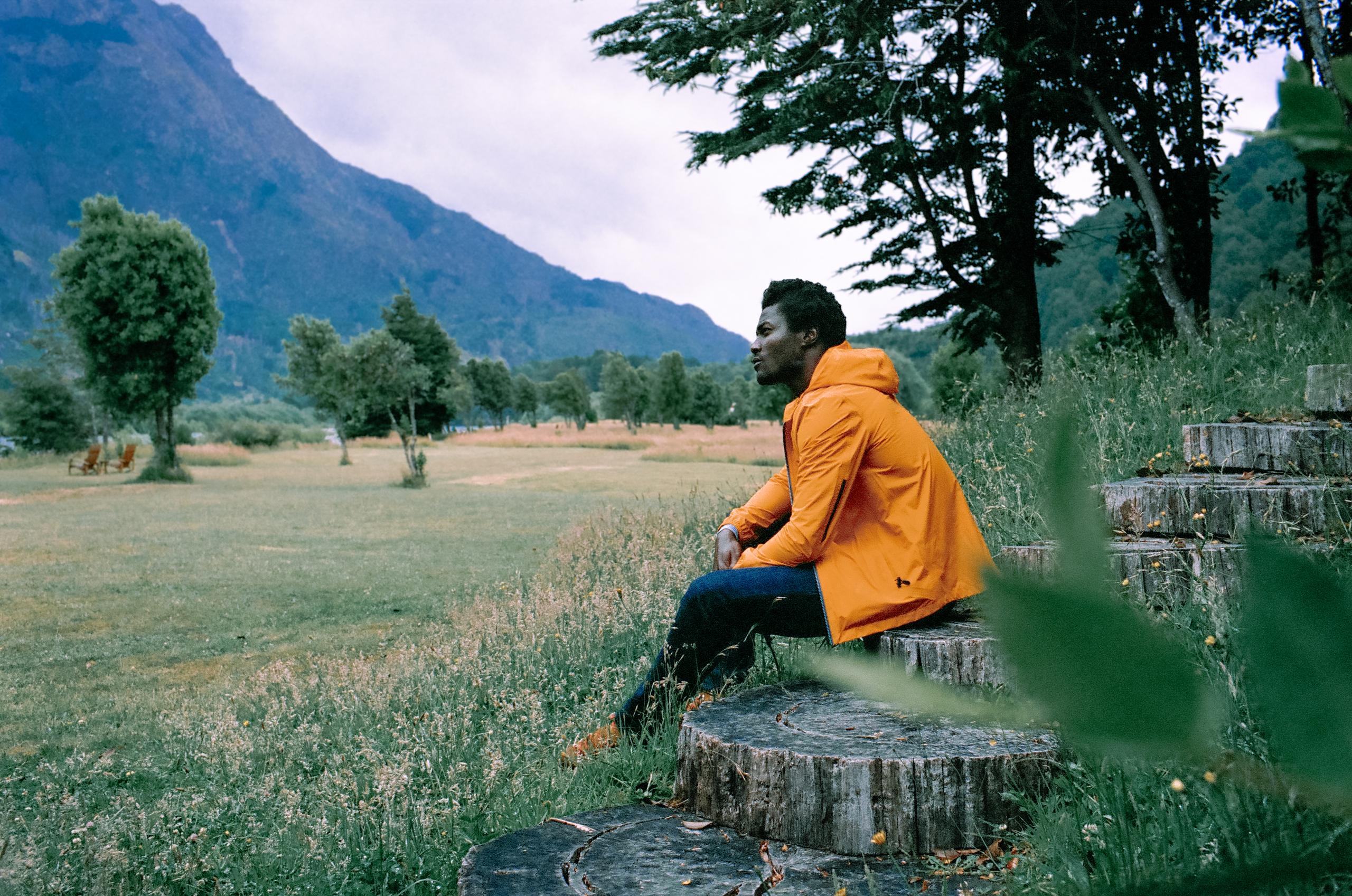 Man in orange Storm Jacket sitting on wood steps looking at open field in Patagonia, Chile