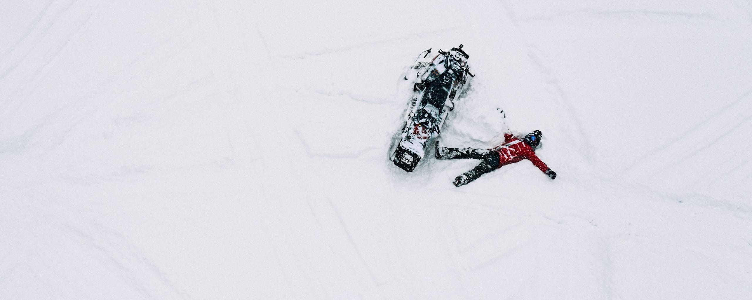 Aerial view of man laying in snow next to snowmobile in Aspen